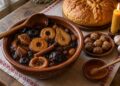 Ошав от сушени сливи, ябълки, круши и смокини в глинена купа до питка, орехи и мед на трапезата за Бъдни вечер