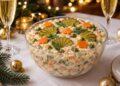 Руска салата в стъклена купа, украсена с моркови, краставички и копър, на празнична новогодишна маса