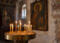 Запалени тънки восъчни свещи в месингов свещник с пясък пред стара икона в българска църква