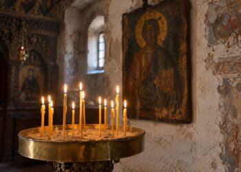 Запалени тънки восъчни свещи в месингов свещник с пясък пред стара икона в българска църква