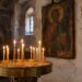 Запалени тънки восъчни свещи в месингов свещник с пясък пред стара икона в българска църква