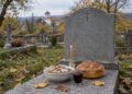 Варено жито, хляб, чаша червено вино и запалена свещ на гроб в селски гробищен парк през есента